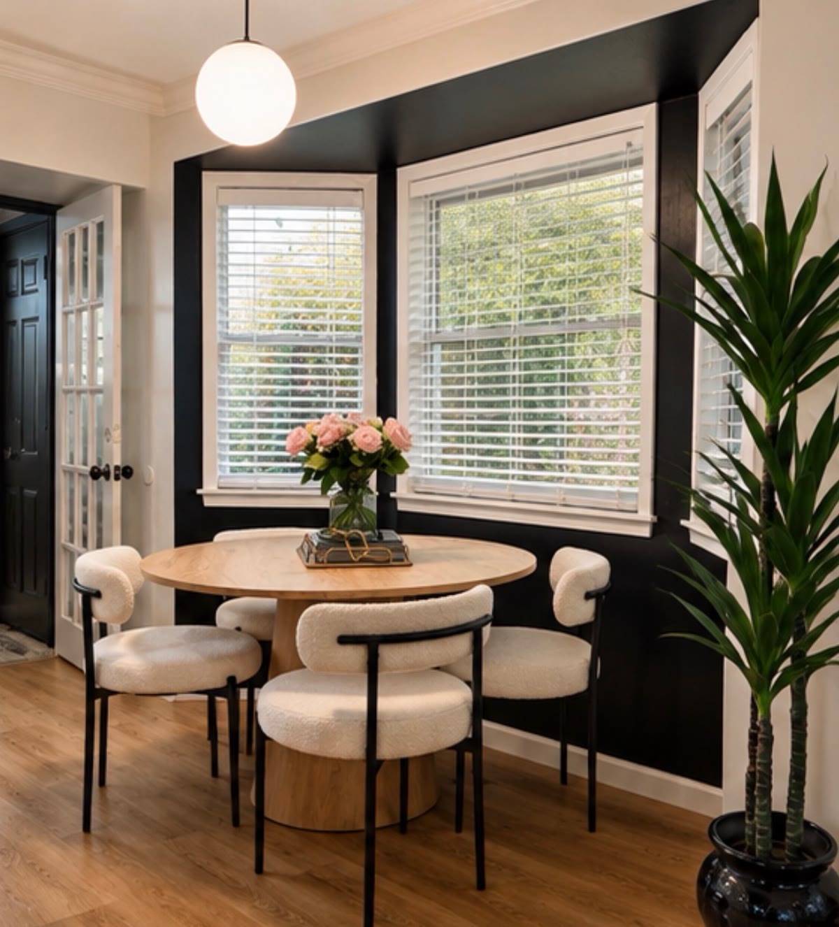 Dining nook with a round wood table, cream chairs, and black accent wall